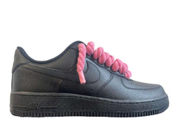 Schwarzer Nike Air Force 1 Sneaker mit pinken, dicken Rope-Schnürsenkeln, die dem klassischen Design des Schuhs einen auffälligen und modernen Akzent verleihen. Der Schuh hat eine matte Oberfläche und eine robuste schwarze Sohle, die für einen markanten Look sorgt.