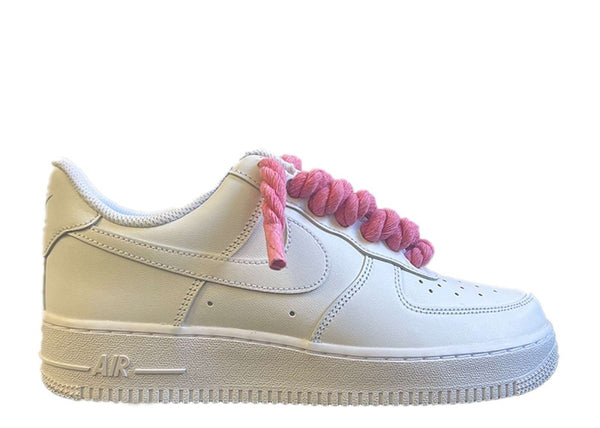 Weißer Nike Air Force 1 Schuh mit pinken, dicken Rope-Schnürsenkeln, die dem klassischen Design des Schuhs einen auffälligen und modernen Akzent verleihen. Der Schuh hat eine matte Oberfläche und eine robuste schwarze Sohle, die für einen markanten Look sorgt.