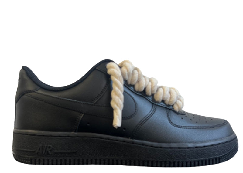 Schwarzer Nike Air Force 1 Sneaker mit cremeweißen, dicken Rope-Schnürsenkeln, die dem klassischen Design des Schuhs einen auffälligen und modernen Akzent verleihen. Der Schuh hat eine matte Oberfläche und eine robuste schwarze Sohle, die für einen markanten Look sorgt.