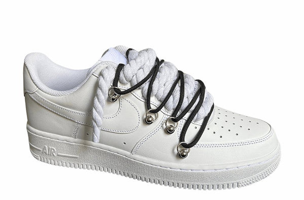 Weißer Nike Air Force 1 Sneaker mit dicken weißen Rope-Schnürsenkeln, kombiniert mit schwarzen Akzent-Schnüren. Der Schuh hat eine matte weiße Oberfläche, Metallösen und eine robuste Sohle, die dem Design einen modernen und markanten Look verleiht, von der Seite.