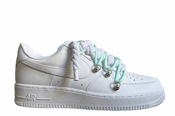 Weißer Nike Air Force 1 Sneaker mit dicken weißen Rope-Schnürsenkeln, kombiniert mit türkisen Akzent-Schnüren. Der Schuh hat eine matte weiße Oberfläche, Metallösen und eine robuste Sohle, die dem Design einen modernen und markanten Look verleiht.