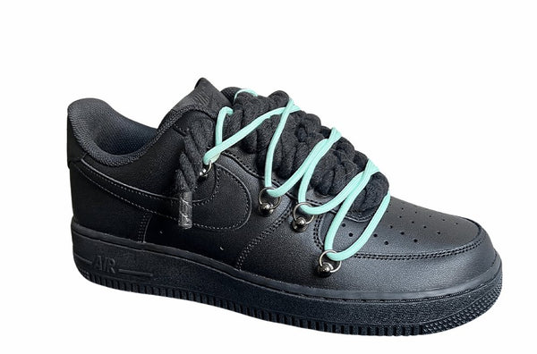 Schwarzer Nike Air Force 1 Sneaker mit dicken schwarzen Rope-Schnürsenkeln, kombiniert mit türkisen Akzent-Schnüren. Der Schuh hat eine matte schwarze Oberfläche, Metallösen und eine robuste Sohle, die dem Design einen modernen und markanten Look verleiht, von der Seite.