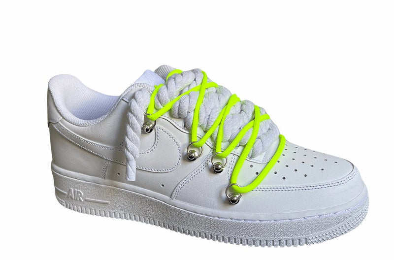 Weißer Nike Air Force 1 Sneaker mit dicken weißen Rope-Schnürsenkeln, kombiniert mit neonfarbenden Akzent-Schnüren. Der Schuh hat eine matte weiße Oberfläche, Metallösen und eine robuste Sohle, die dem Design einen modernen und markanten Look verleiht, von der Seite.