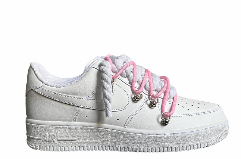 Weißer Nike Air Force 1 Sneaker mit dicken weißen Rope-Schnürsenkeln, kombiniert mit pinken Akzent-Schnüren. Der Schuh hat eine matte weiße Oberfläche, Metallösen und eine robuste Sohle, die dem Design einen modernen und markanten Look verleiht.