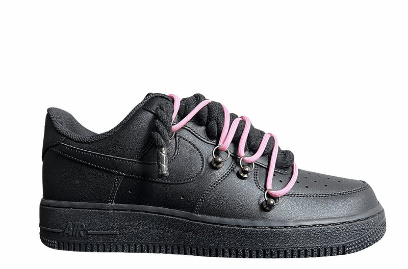 Schwarzer Nike Air Force 1 Sneaker mit dicken schwarzen Rope-Schnürsenkeln, kombiniert mit pinken Akzent-Schnüren. Der Schuh hat eine matte schwarze Oberfläche, Metallösen und eine robuste Sohle, die dem Design einen modernen und markanten Look verleiht.