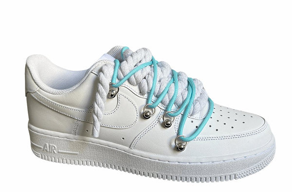 Weißer Nike Air Force 1 Sneaker mit dicken weißen Rope-Schnürsenkeln, kombiniert mit blauen Akzent-Schnüren. Der Schuh hat eine matte weiße Oberfläche, Metallösen und eine robuste Sohle, die dem Design einen modernen und markanten Look verleiht, von der Seite.