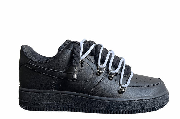 Schwarzer Nike Air Force 1 Sneaker mit dicken schwarzen Rope-Schnürsenkeln, kombiniert mit weißen Akzent-Schnüren. Der Schuh hat eine matte schwarze Oberfläche, Metallösen und eine robuste Sohle, die dem Design einen modernen und markanten Look verleiht.