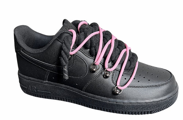 Schwarzer Nike Air Force 1 Sneaker mit dicken schwarzen Rope-Schnürsenkeln, kombiniert mit pinken Akzent-Schnüren. Der Schuh hat eine matte schwarze Oberfläche, Metallösen und eine robuste Sohle, die dem Design einen modernen und markanten Look verleiht, von der Seite