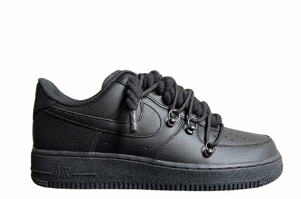 Schwarzer Nike Air Force 1 Sneaker mit dicken schwarzen Rope-Schnürsenkeln, kombiniert mit schwarzen Akzent-Schnüren. Der Schuh hat eine matte schwarze Oberfläche, Metallösen und eine robuste Sohle, die dem Design einen modernen und markanten Look verleiht.