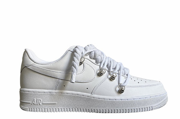 Weißer Nike Air Force 1 Sneaker mit dicken weißen Rope-Schnürsenkeln, kombiniert mit weißen Akzent-Schnüren. Der Schuh hat eine matte weiße Oberfläche, Metallösen und eine robuste Sohle, die dem Design einen modernen und markanten Look verleiht.