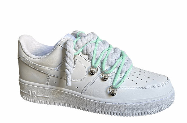 Weißer Nike Air Force 1 Sneaker mit dicken weißen Rope-Schnürsenkeln, kombiniert mit türkisen Akzent-Schnüren. Der Schuh hat eine matte weiße Oberfläche, Metallösen und eine robuste Sohle, die dem Design einen modernen und markanten Look verleiht, von der Seite.