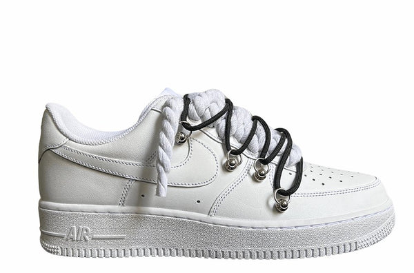 Weißer Nike Air Force 1 Sneaker mit dicken weißen Rope-Schnürsenkeln, kombiniert mit schwarzen Akzent-Schnüren. Der Schuh hat eine matte weiße Oberfläche, Metallösen und eine robuste Sohle, die dem Design einen modernen und markanten Look verleiht.