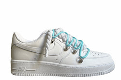 Weißer Nike Air Force 1 Sneaker mit dicken weißen Rope-Schnürsenkeln, kombiniert mit blauen Akzent-Schnüren. Der Schuh hat eine matte weiße Oberfläche, Metallösen und eine robuste Sohle, die dem Design einen modernen und markanten Look verleiht.