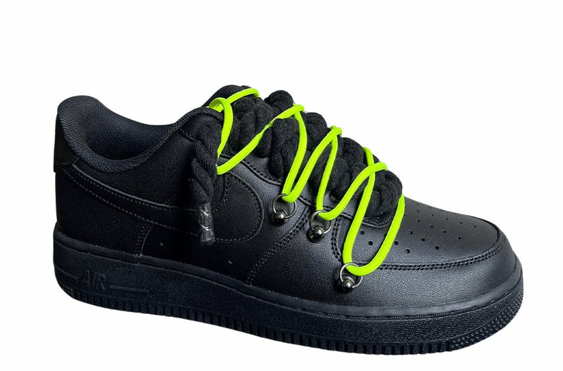 Schwarzer Nike Air Force 1 Sneaker mit dicken schwarzen Rope-Schnürsenkeln, kombiniert mit neonfarbenden Akzent-Schnüren. Der Schuh hat eine matte schwarze Oberfläche, Metallösen und eine robuste Sohle, die dem Design einen modernen und markanten Look verleiht, von der Seite